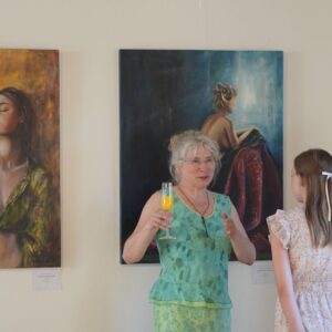 Frau und Mädchenunterhalten sich vor Gemälden in einer Ausstellung. Frau hält ein Getränk.