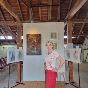 Frau in roter Hose steht vor Gemälden in einer Kunstgalerie mit Holzbalken. Die Bilder sind von Künstler Yvonne Brückner Sächsische Schweiz