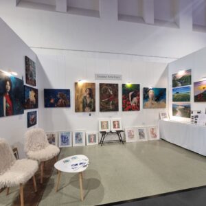 Kunstausstellung mit Gemälden an weißen Wänden, zwei flauschige Stühle und ein Tisch davor.