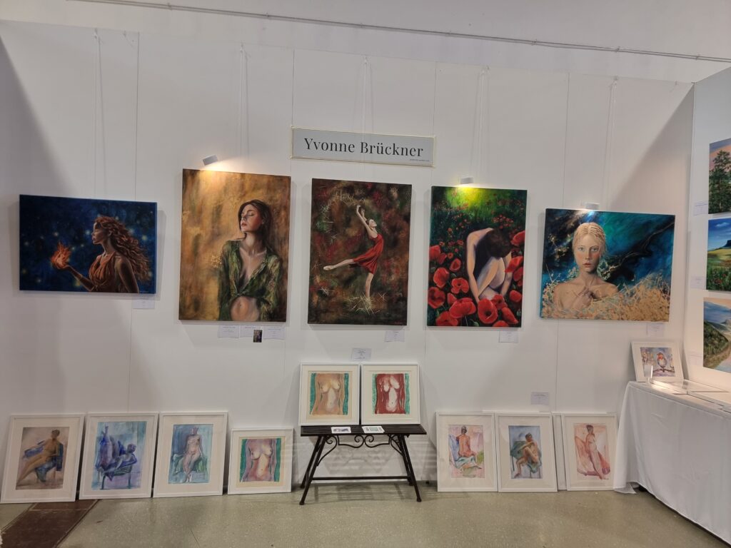 Kunstausstellung mit Gemälden von Yvonne Brückner an weißen Wänden, darunter Porträts und Fantasiebilder.