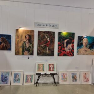 Kunstausstellung mit Gemälden von Yvonne Brückner an weißen Wänden, darunter Porträts und Fantasiebilder.