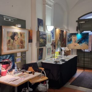 Verkaufsausstellung mit Gemälden an Wänden und auf Tischen, Gewölbedecke, Arbeitsmaterialien. Arbeiten von Künstler Yvonne Brückner.